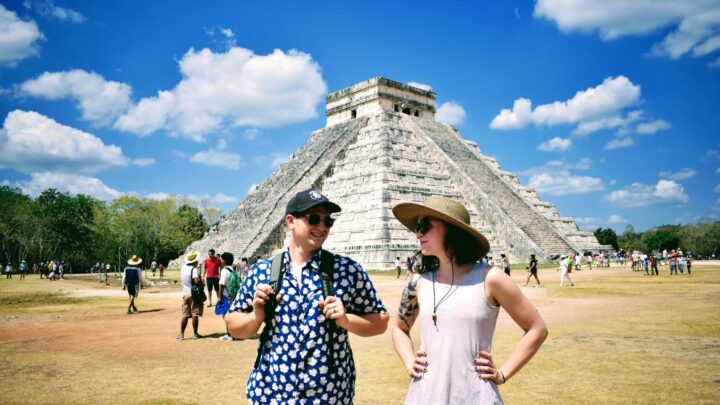Visitors enjoying a private tour at the archaeological site of Chichen Itza, surrounded by ancient ruins and blue skies, by Carey Tours.