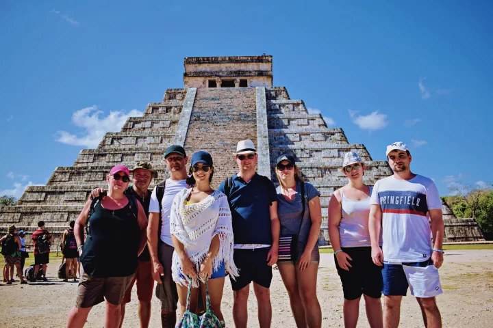 Group enjoying a private tour at the archaeological site of Chichén Itzá, surrounded by ancient ruins and a clear blue sky by Carey Tours.