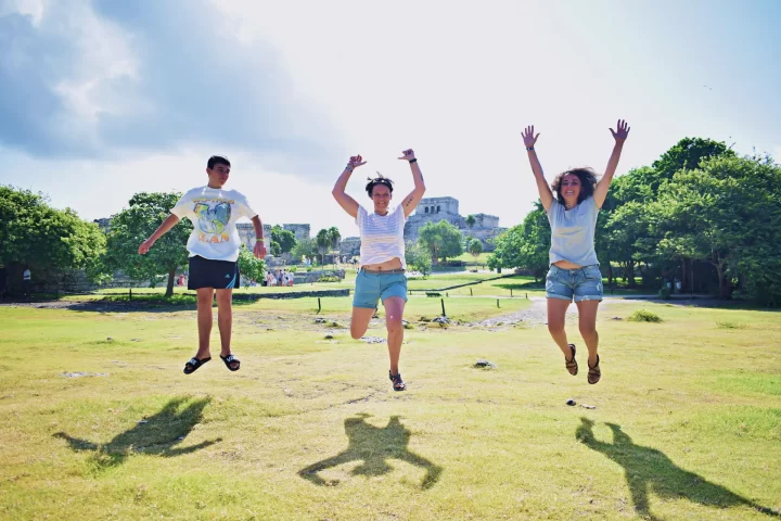 Group of cheerful travelers jumping in the air at an archaeological site in Tulum, embracing the experience by Carey Tours.
