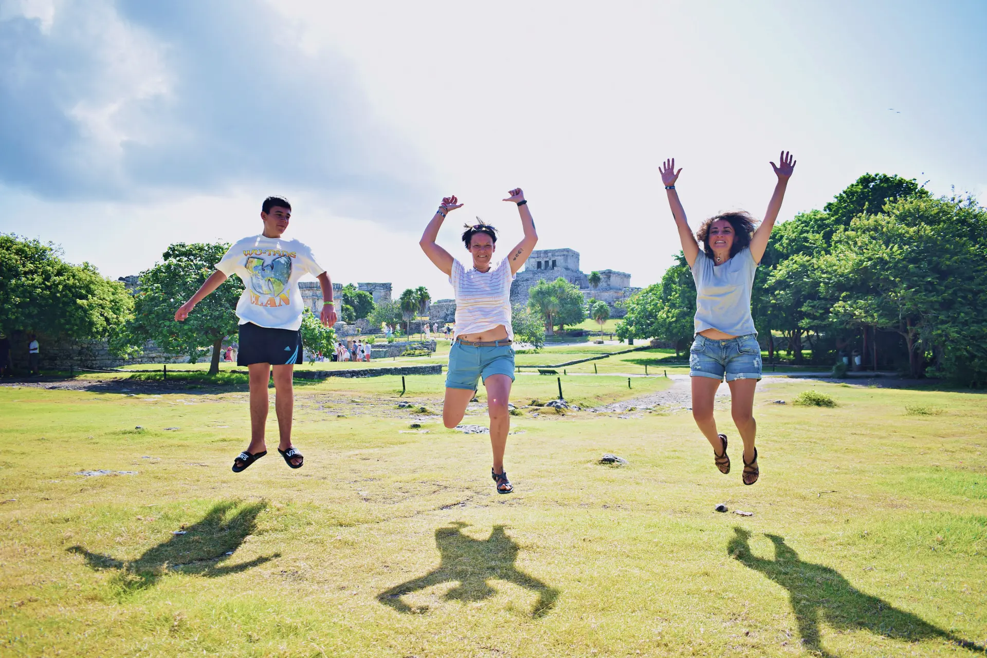 Group of cheerful travelers jumping in the air at an archaeological site in Tulum, embracing the experience by Carey Tours.