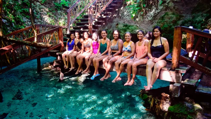 Group of women enjoying a tranquil moment while dipping their feet in a crystal-clear cenote during a private tour by Carey Tours.