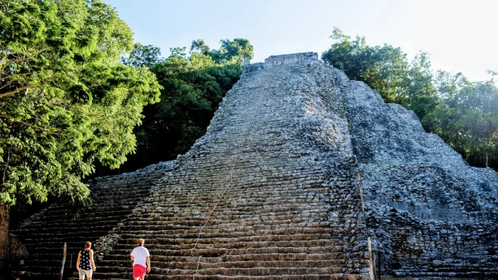 Visitors ascending the ancient steps of a Mayan pyramid surrounded by lush jungle, enjoying a private tour experience by Carey Tours