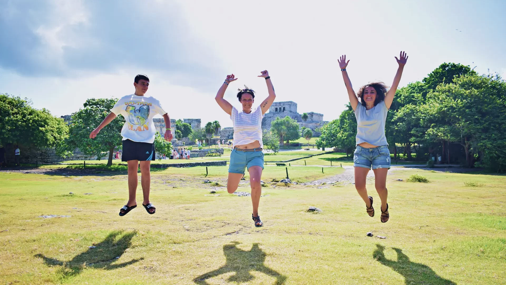 Group of cheerful travelers jumping in the air at an archaeological site in Tulum, embracing the experience by Carey Tours.